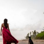 Pet Insurance - A woman in a red dress walking on the beach with a dog