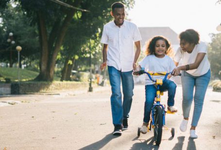 Family Time - Man Standing Beside His Wife Teaching Their Child How to Ride Bicycle