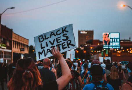 Event Changes - Back view of group of demonstrators showing banners with slogans in downtown under dark blue sky at night