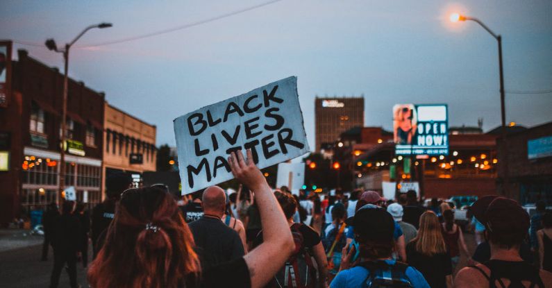 Event Changes - Back view of group of demonstrators showing banners with slogans in downtown under dark blue sky at night